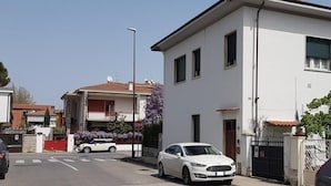 A residential street with houses, a white car parked on the side, and a stop sign. - La Coccinella Guest House (Pisa)