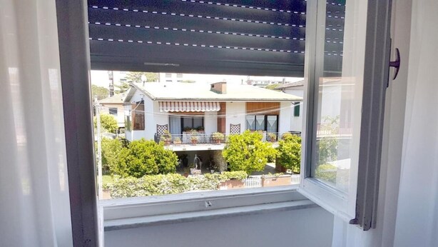 A window with a view of a residential area, including a house with a balcony and greenery. - La Coccinella Guest House (Pisa)