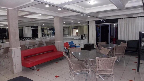 En rummelig hotellobby med en rød sofa, fletstole, et bord med glasplade og et køkkenområde i baggrunden.