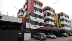 A multi-story hotel with a red and white facade, several balconies, and a parking area with cars. - Hotel Rota Do Pantanal (Presidente Prudente)