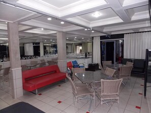 Un vaste espace dédié à la salle à manger, avec un canapé rouge, des chaises en osier et une grande table.