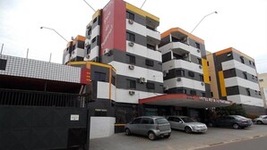 Et hotel med flere etager, en rød og hvid facade, adskillige balkoner og en parkeringsplads med flere biler.