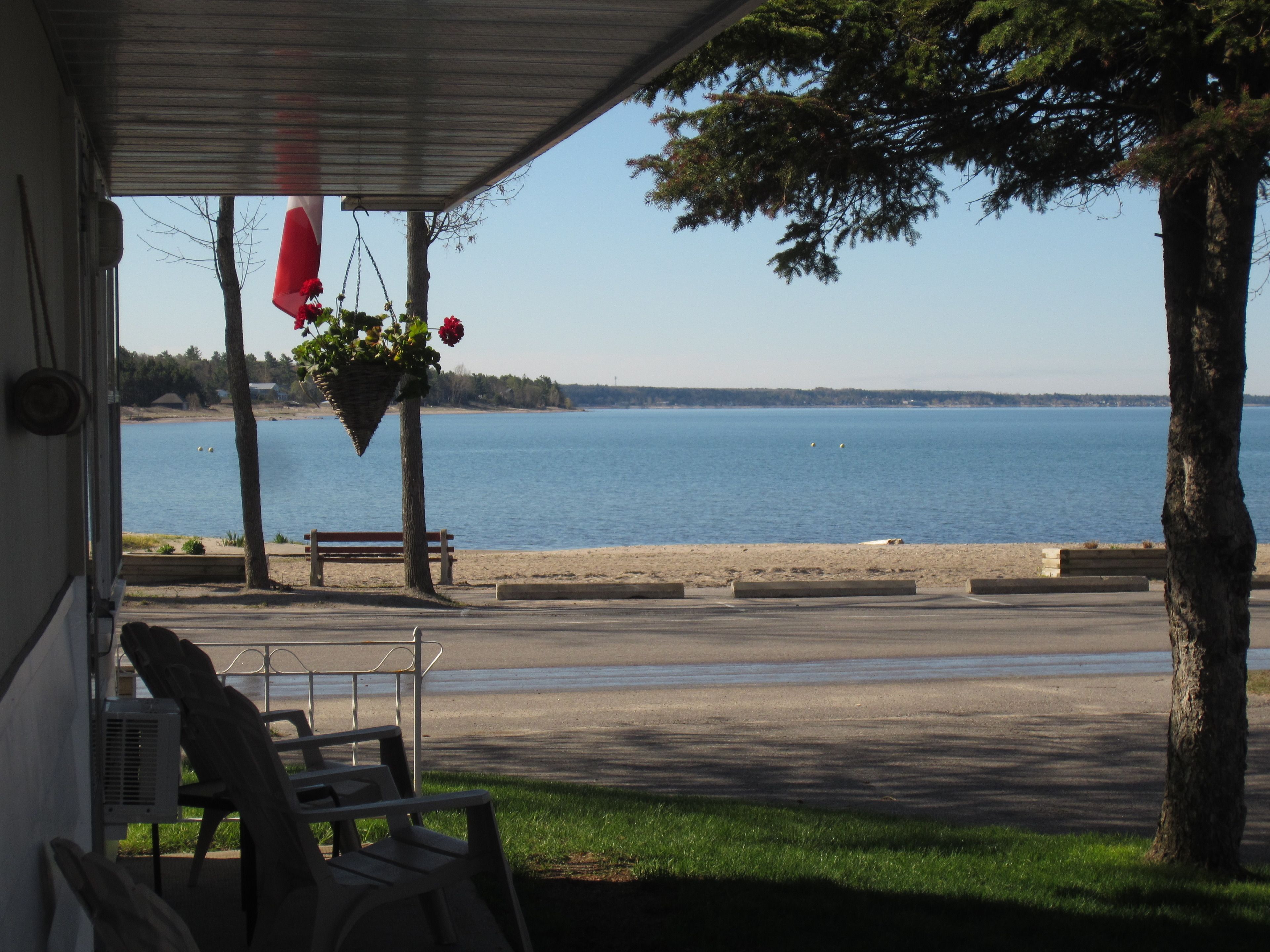 Une véranda abritée, dotée d’un banc et de chaises, qui offre une vue sur une étendue d’eau calme et une rive lointaine.