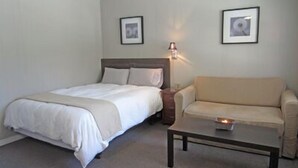 A bedroom with a bed, a bedside table, a lamp, a sofa, and a coffee table. - Balm Beach Resort & Motel (Tiny)