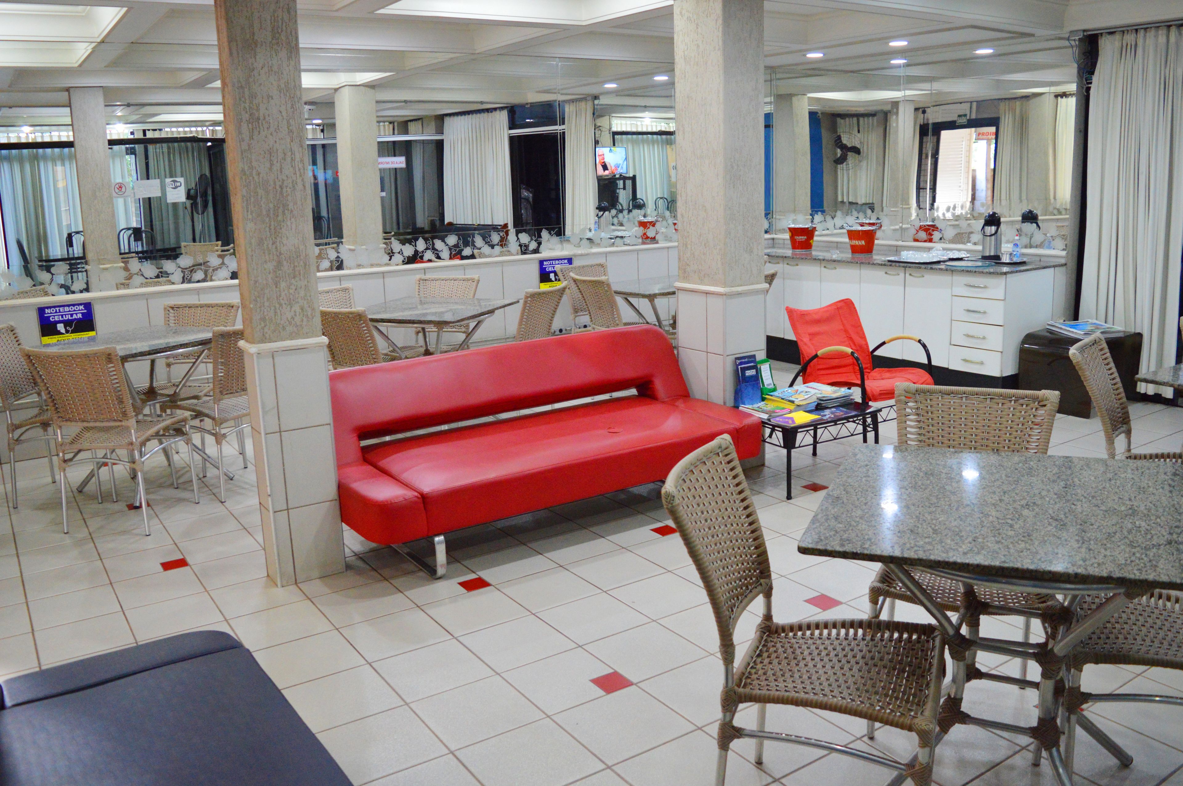 A hotel lobby with a red sofa, wicker chairs, a granite table, and a kitchen area with a sink and counter.