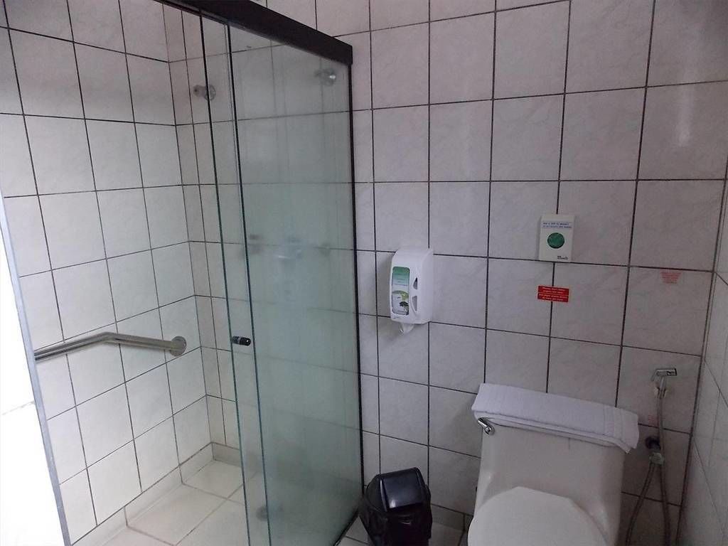 A bathroom with a glass shower enclosure, a white toilet, and a hand dryer.
