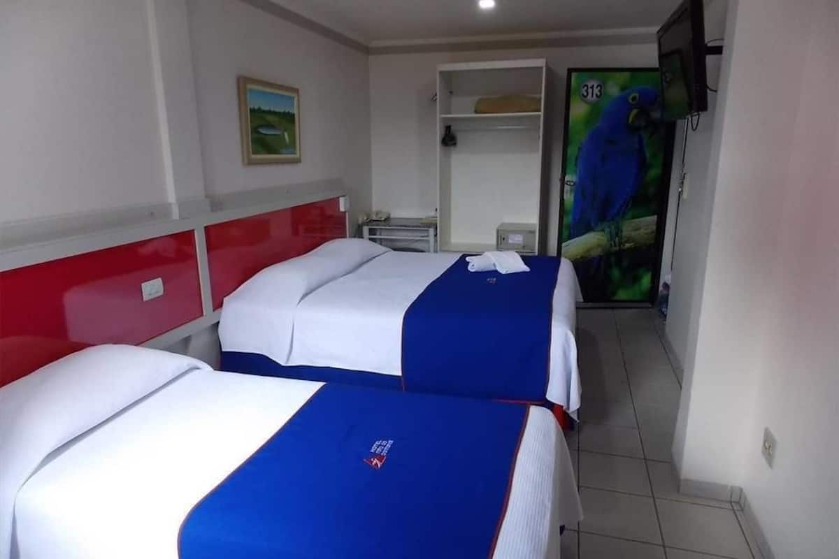 Une chambre d’hôtel avec deux lits, une tête de lit rouge, un tableau au mur et un téléviseur fixé au mur.