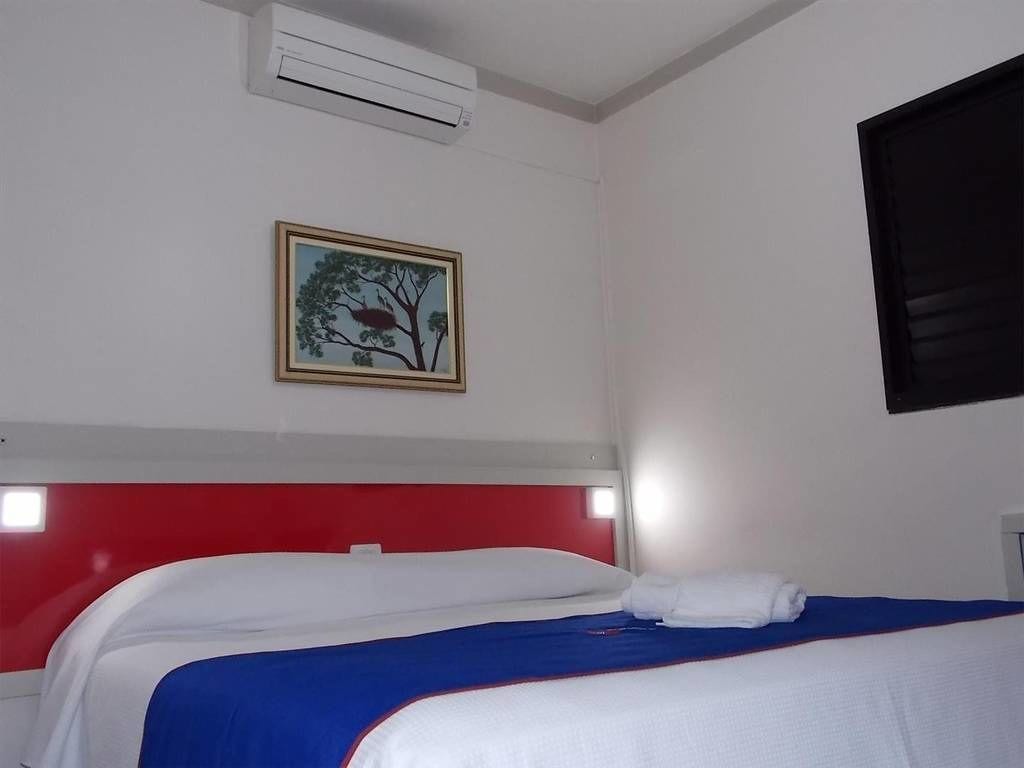 A hotel room with two beds, a red headboard, a framed picture on the wall, and an air conditioning unit.