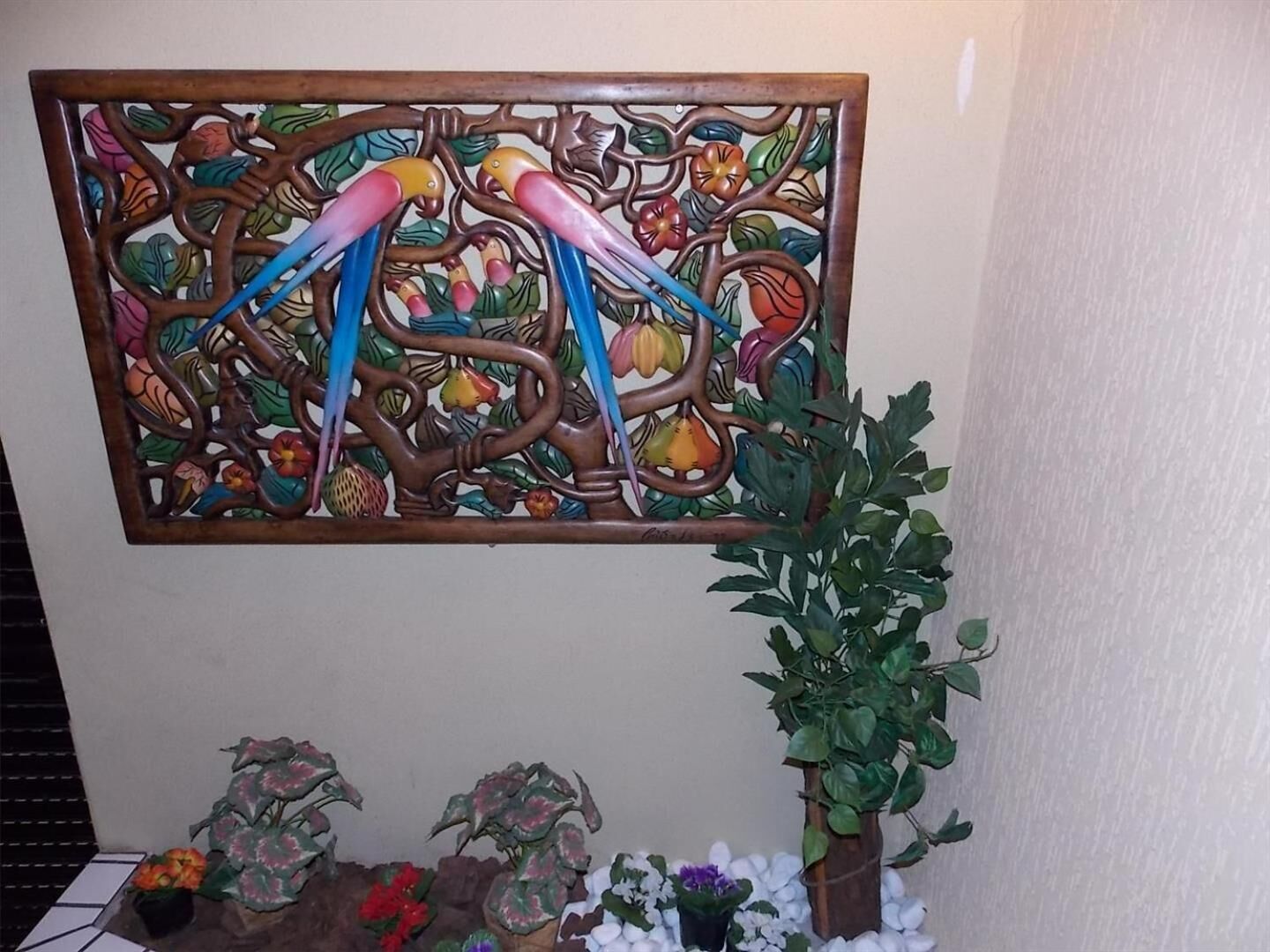 Ein dekoratives Wandpaneel mit Baum und Vögeln, umgeben von Topfpflanzen.