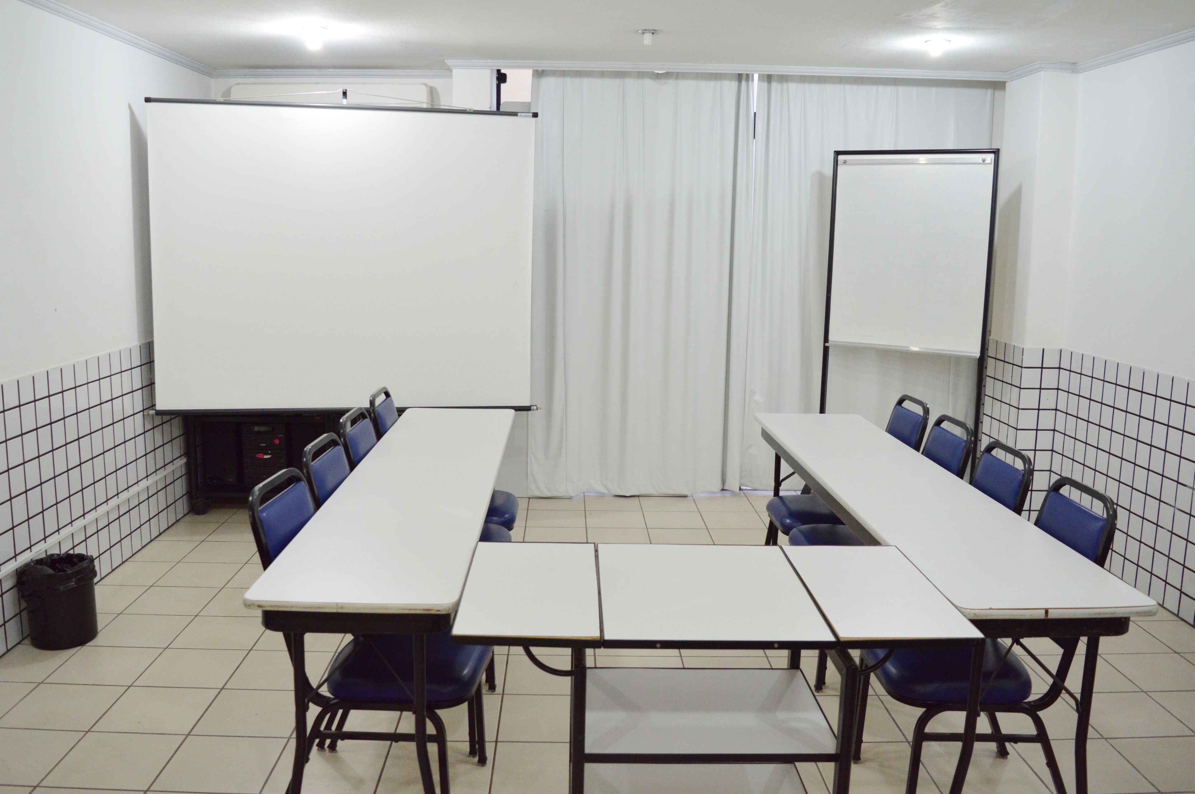A conference room with a long table, blue chairs, a whiteboard, and a projector screen.