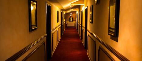 A long, narrow hallway with a red carpet, flanked by walls with framed pictures and light fixtures.