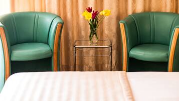 Habitación de hotel con dos sillones verdes tapizados, una mesita con un jarrón de flores y una cama con colcha a rayas.