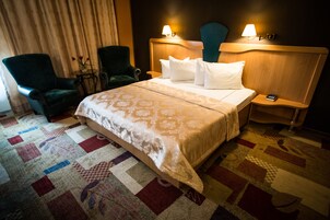 Una habitación de hotel con una cama, dos sillas, una mesita de noche y una lámpara.