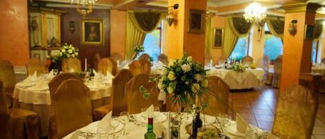 A banquet hall with round tables set for dining, featuring white tablecloths, gold chairs, and floral centerpieces.