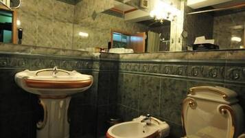 Un baño con lavamanos pedestal, dos inodoros y un espejo.