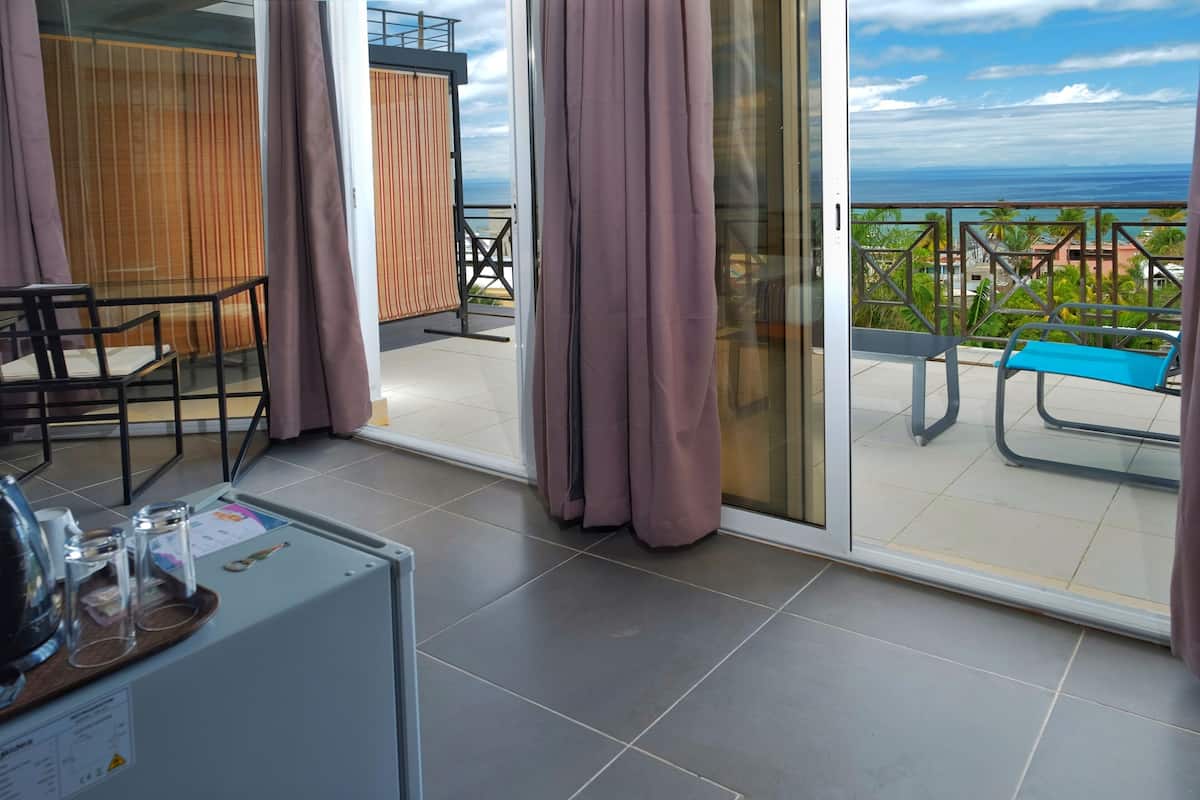 Un balcón con vista al mar, una mesa con sillas y una tumbona azul.