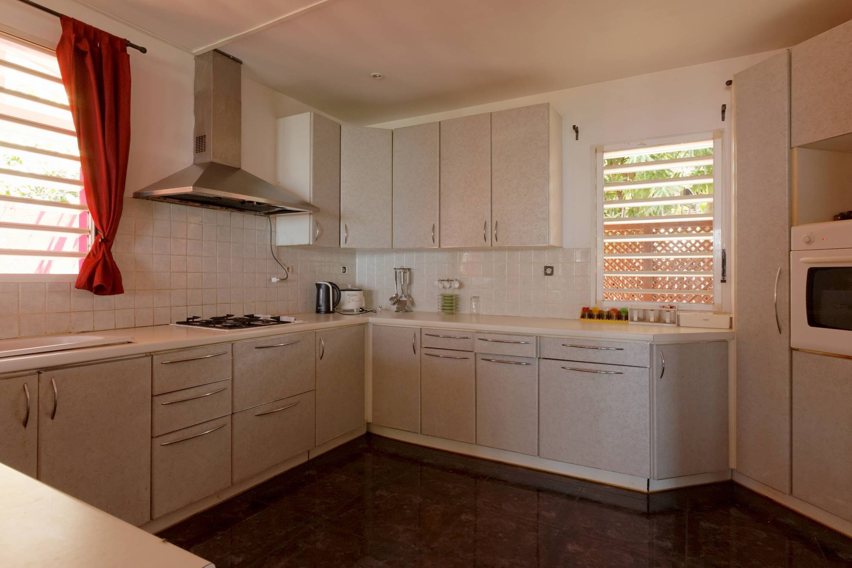A compact kitchen with white cabinets, a gas stove, a range hood, and a window with a view of greenery.