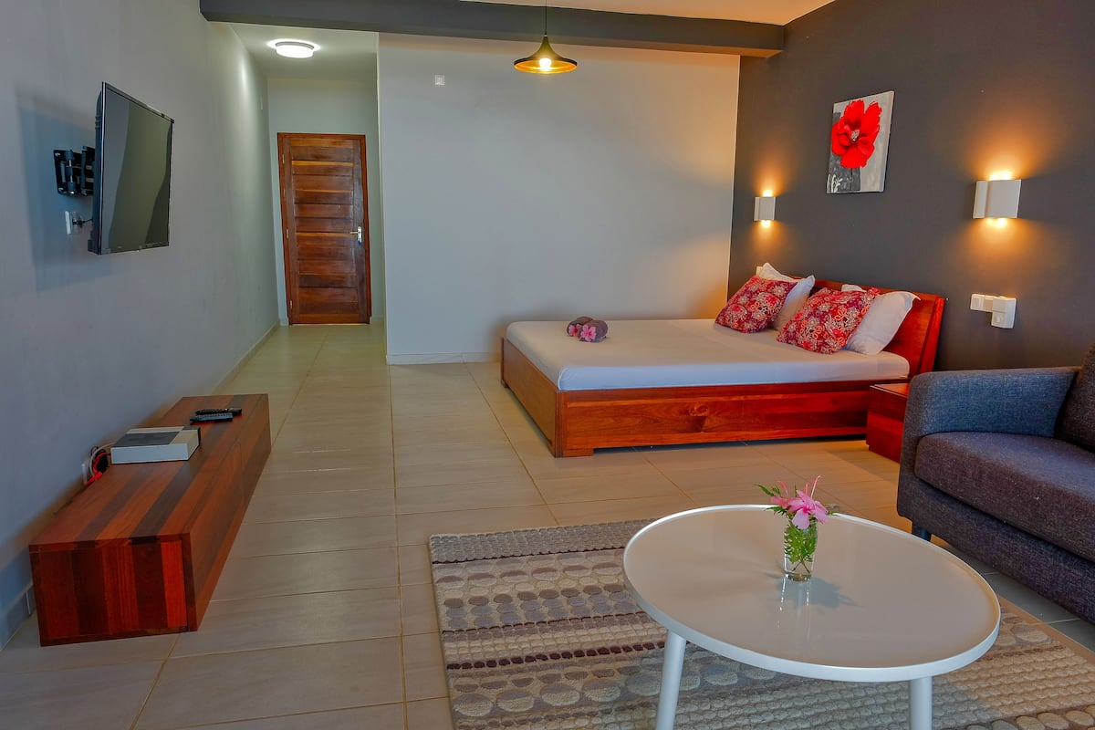 Una sala moderna con un sofá, una mesa de centro, una cama con ropa de cama roja y un televisor fijado a la pared.