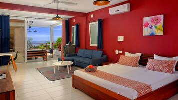 A hotel room with a large bed, a sofa, a desk, and a view of the ocean.