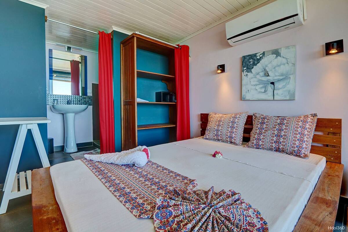 Un dormitorio con cama, mesita de noche, armario, ventana con cortinas, aire acondicionado instalado en la pared y un cuadro.