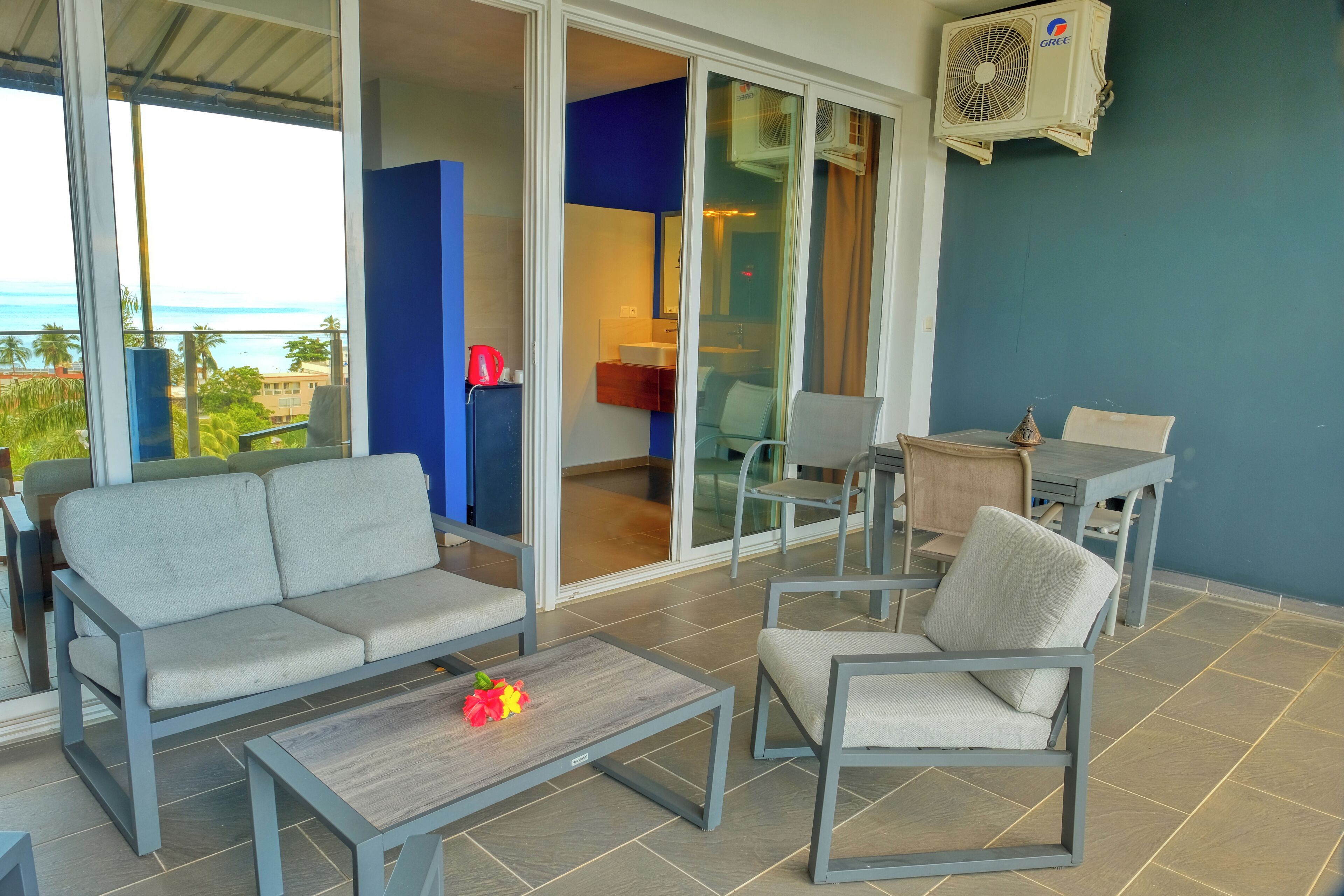 A balcony with a sofa, chairs, a table, and an air conditioning unit.
