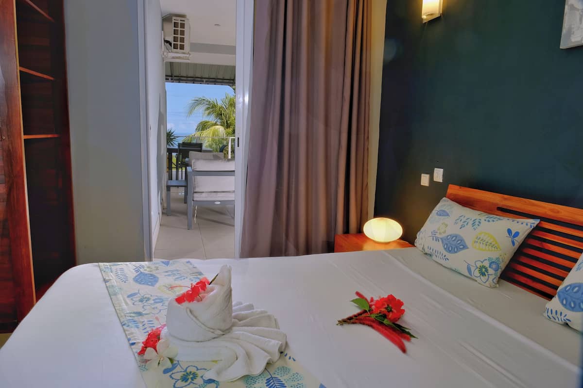 Habitación de hotel con cama, mesita de noche, lámpara, ventana con cortinas y vistas al exterior.