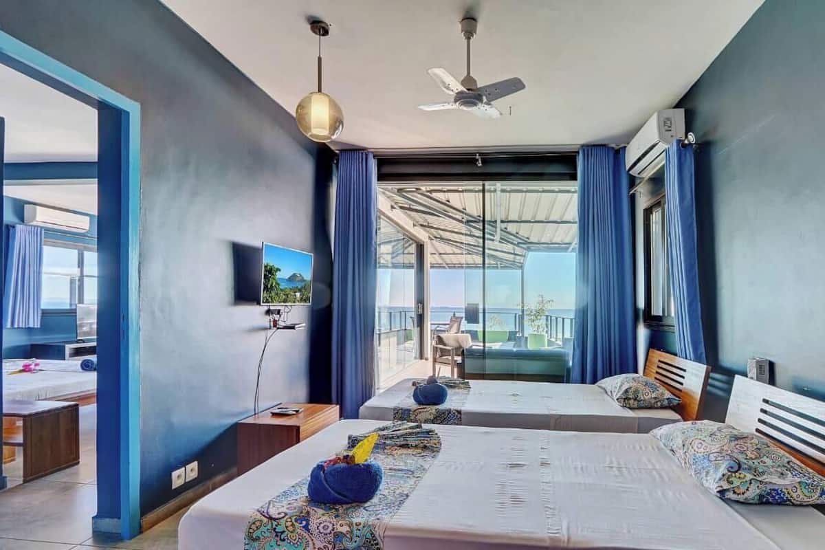 Habitación de hotel con dos camas, ventilador de techo, televisión y balcón con vistas.