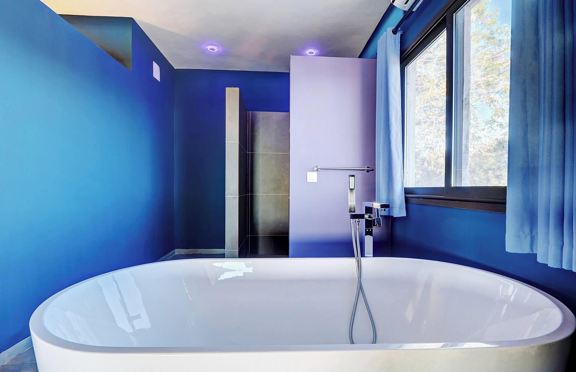 Une salle de bain moderne avec une grande baignoire, un espace douche et une fenêtre avec des rideaux.