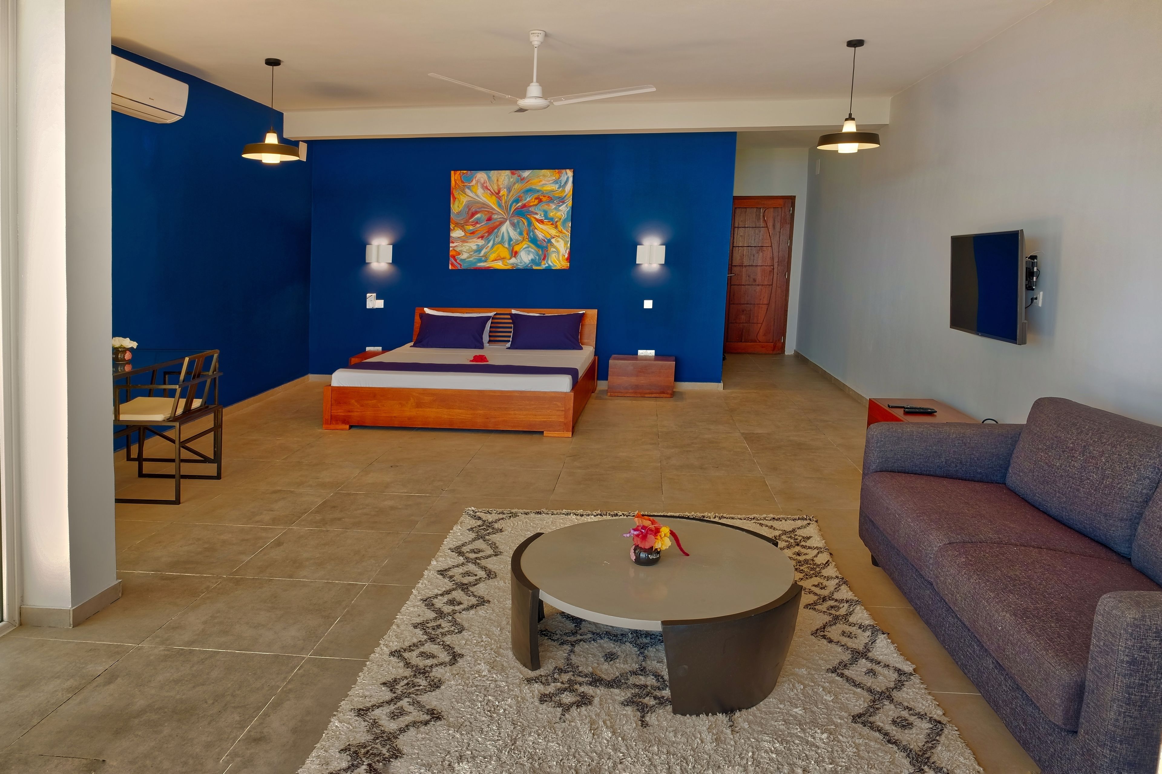 Una habitación de hotel moderna con una cama grande, un sofá, una mesa de centro redonda y un área de comedor con sillas.