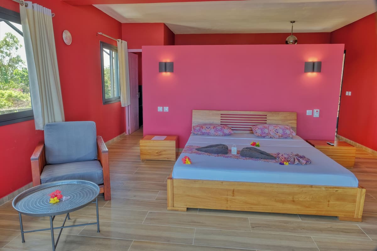 Un dormitorio con cama de madera, una silla, una mesita y una ventana con cortinas.