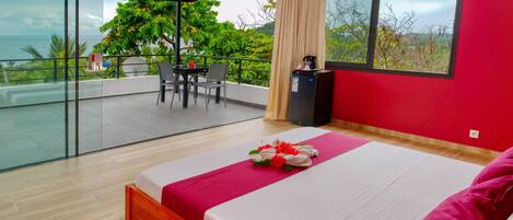 A modern hotel room with a large bed, a balcony with a table and chairs, and a view of the sea.