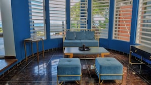 Habitación con pared azul, un sofá, dos otomanas, una mesa de centro y vistas a palmeras.