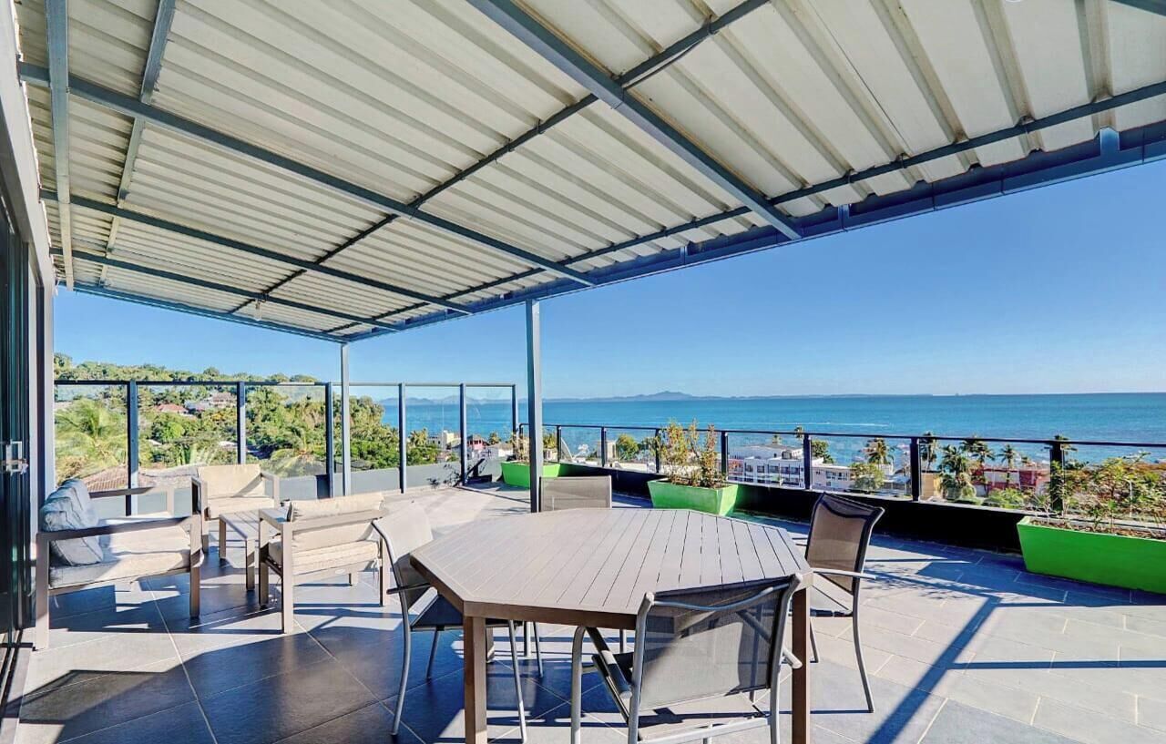 An outdoor terrace with a table and chairs, a covered area, and a view of the sea.