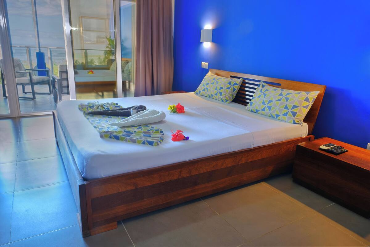 Habitación de hotel con una cama grande, cabecera de madera, mesita de noche y vistas al exterior.