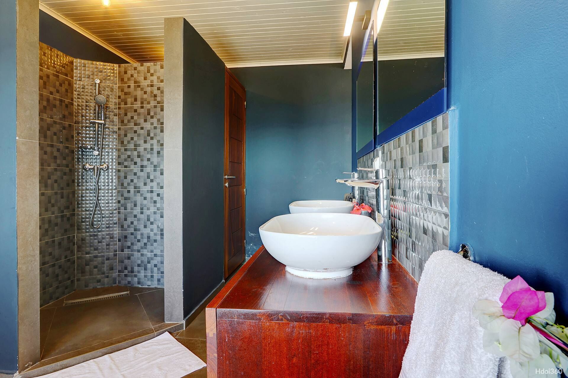 Un baño moderno con un espejo grande, dos lavamanos, zona de ducha y tocador de madera.
