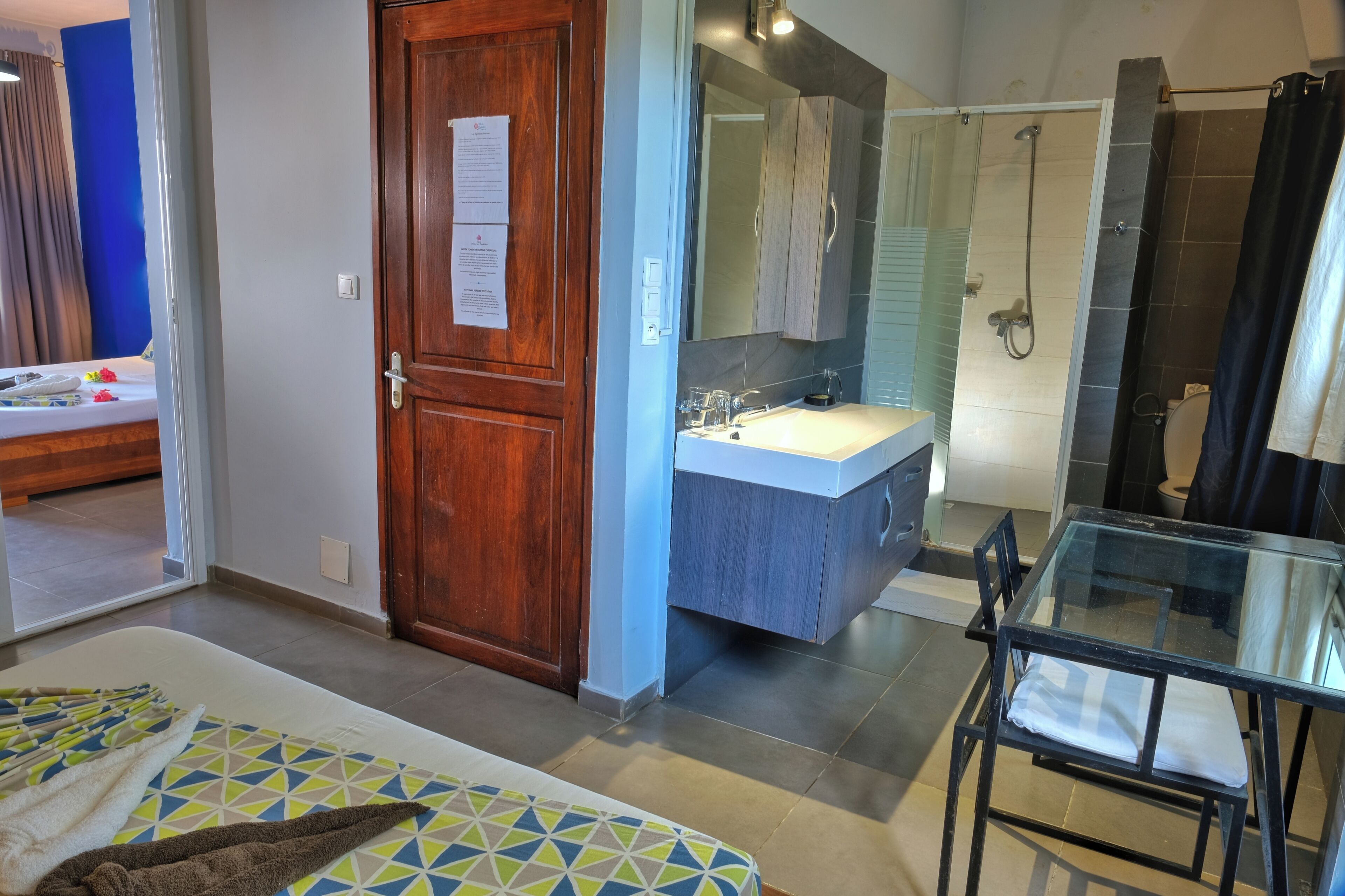 A hotel room with a bed, a glass table, a bathroom with a shower, and a sink.