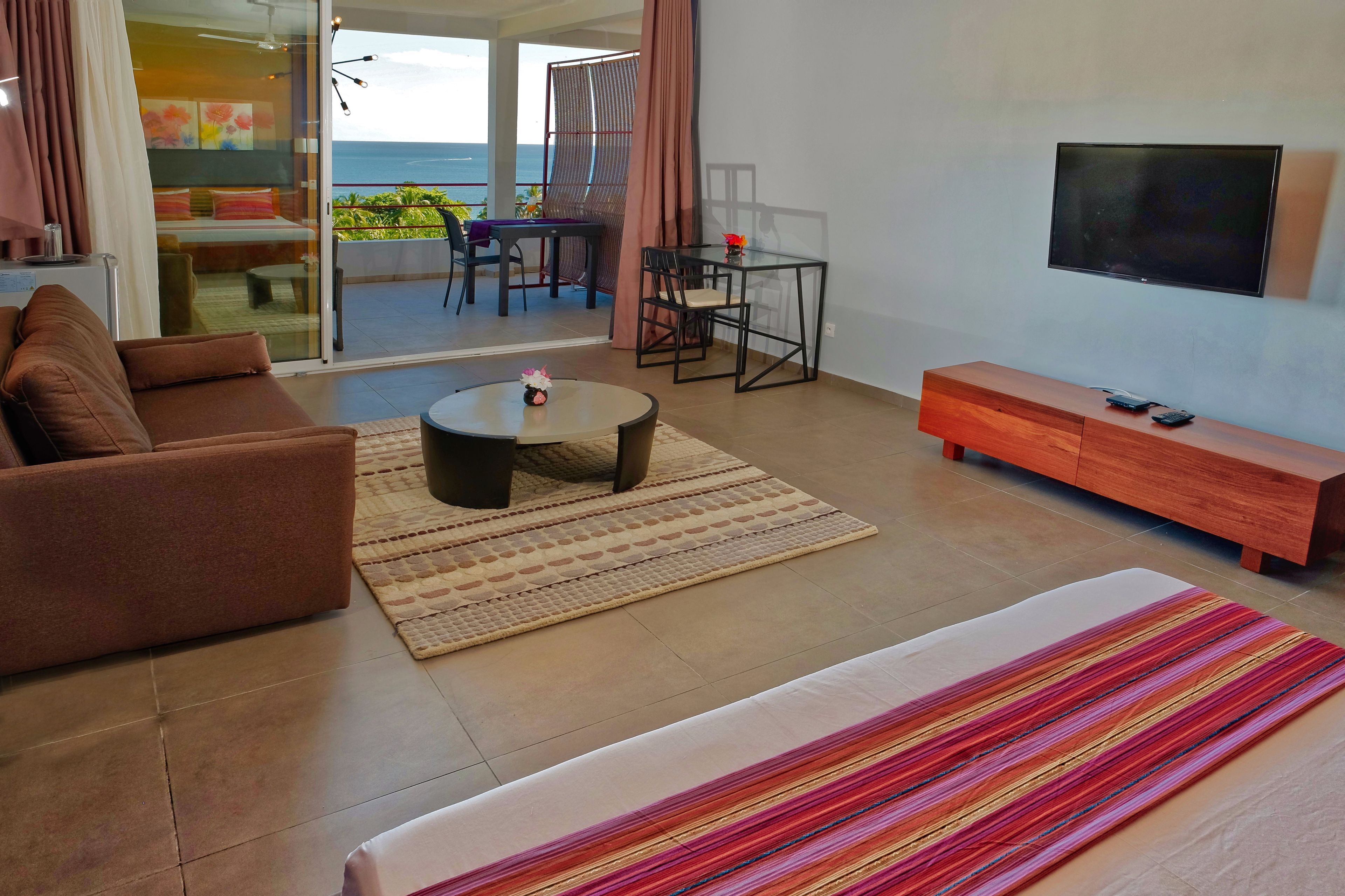 A modern living room with a sofa, a coffee table, a TV, and a view of the sea.