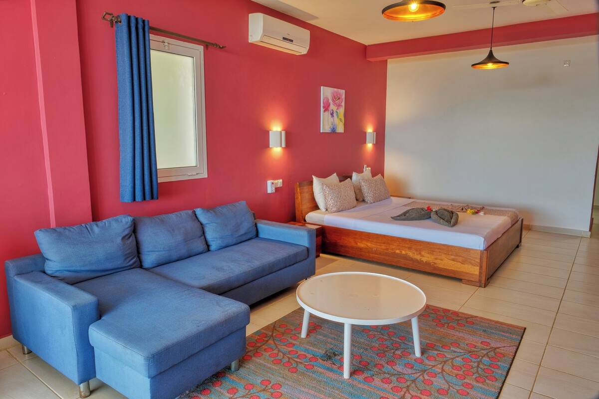 Una habitación con un sofá azul, una cama, una mesa redonda y un tapete estampado.