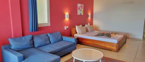 Una habitación con un sofá azul, una cama, una mesa redonda y un tapete estampado.