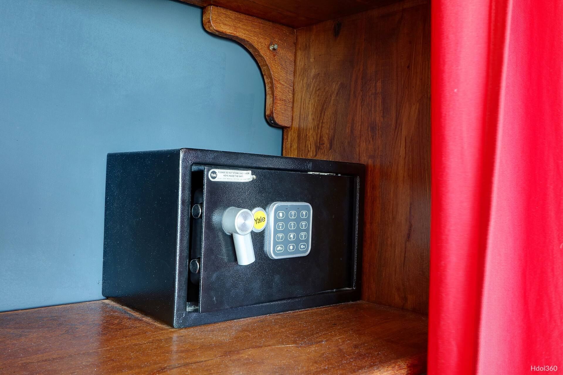 A black safe with a Yale lock and keypad on a wooden shelf.