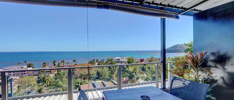 A balcony with a view of the sea, a table, and chairs.