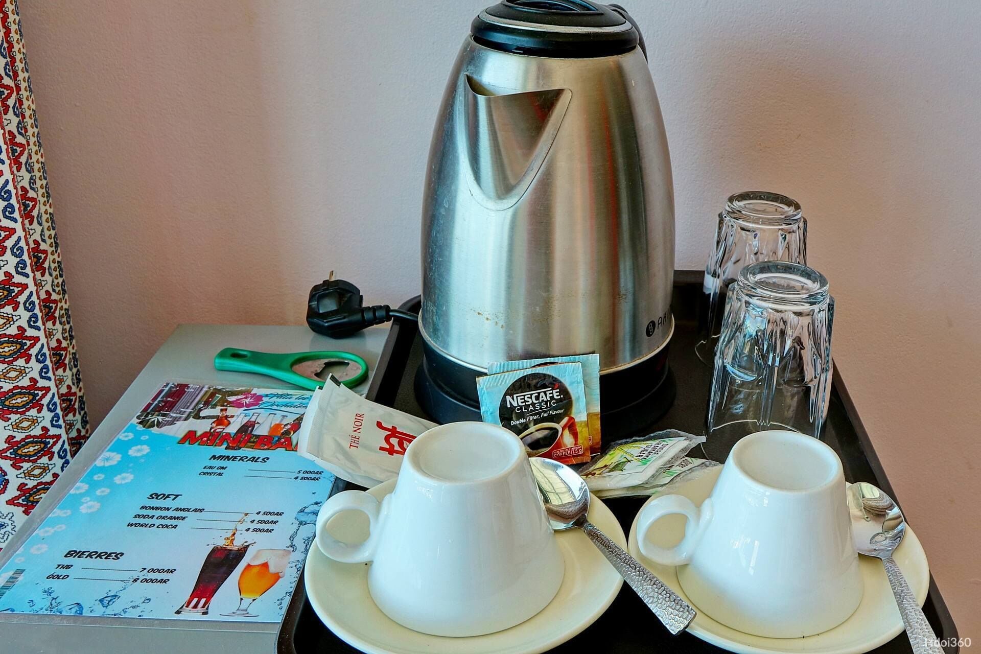 A coffee maker, two cups, a spoon, a packet of Nescafe, and a menu on a table.