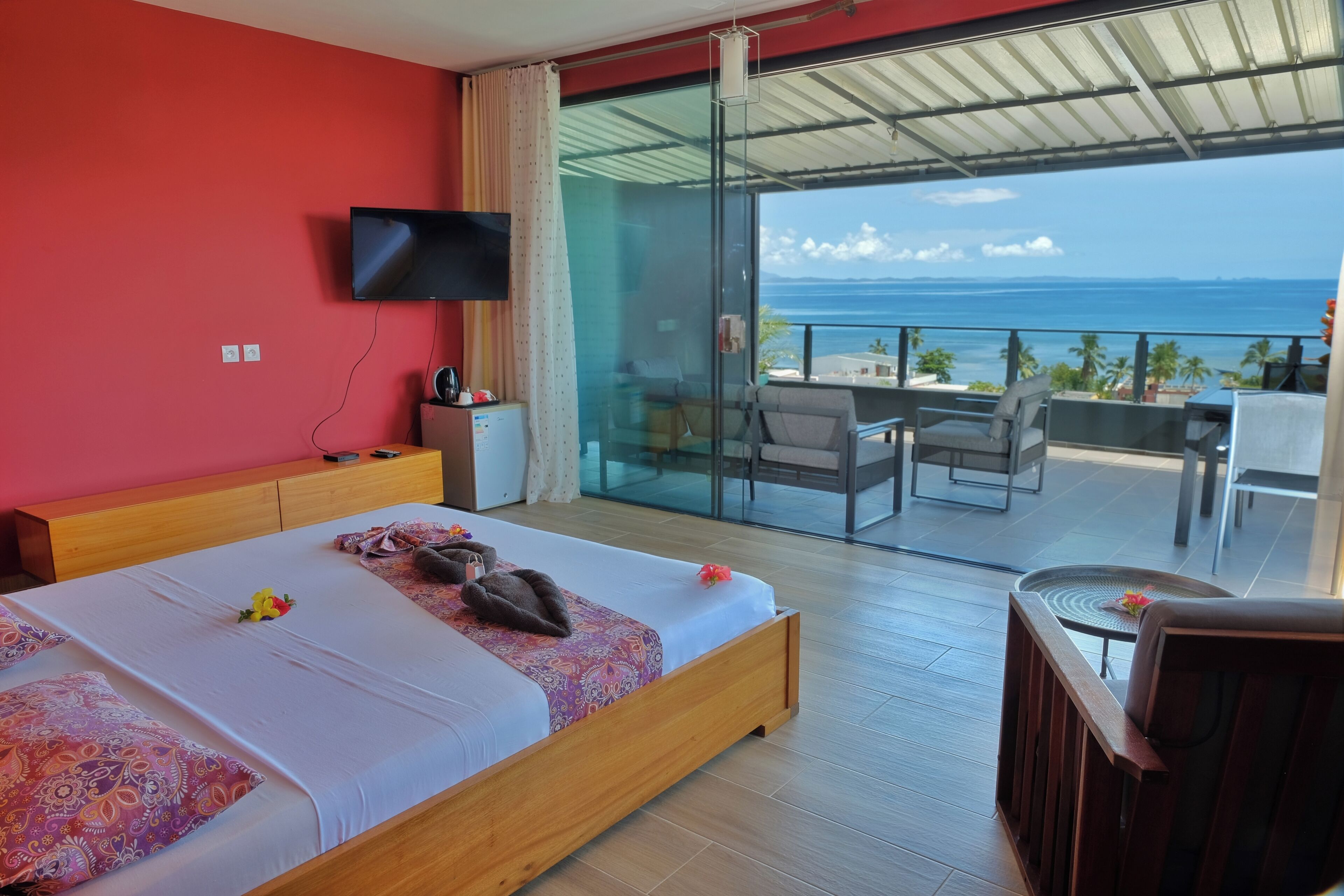 Een hotelkamer met een bed, een televisie, een balkon met tafel en stoelen, en uitzicht op de oceaan.