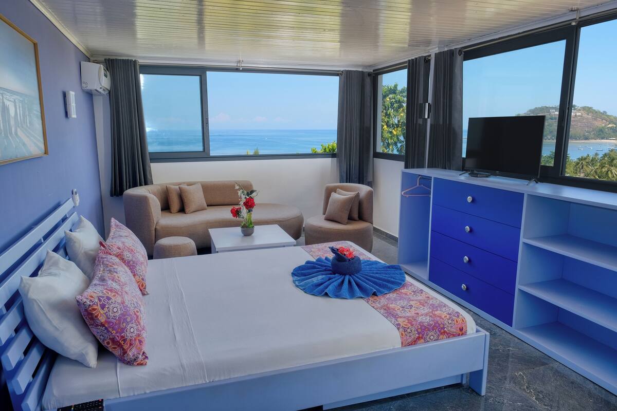 Habitación de hotel con cama, sofá, televisión y vista al mar.