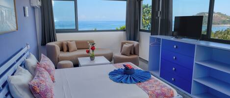 Habitación de hotel con cama, sofá, televisión y vista al mar.