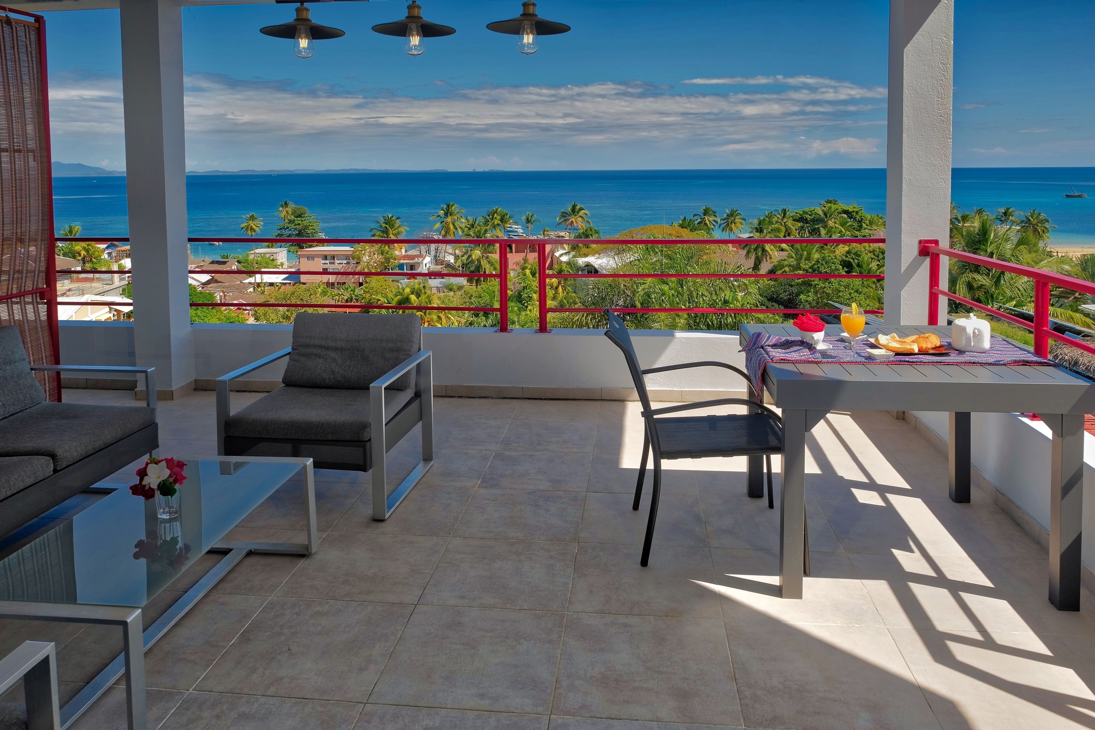 A balcony with a view of the ocean, furnished with a table, chairs, and a sofa.