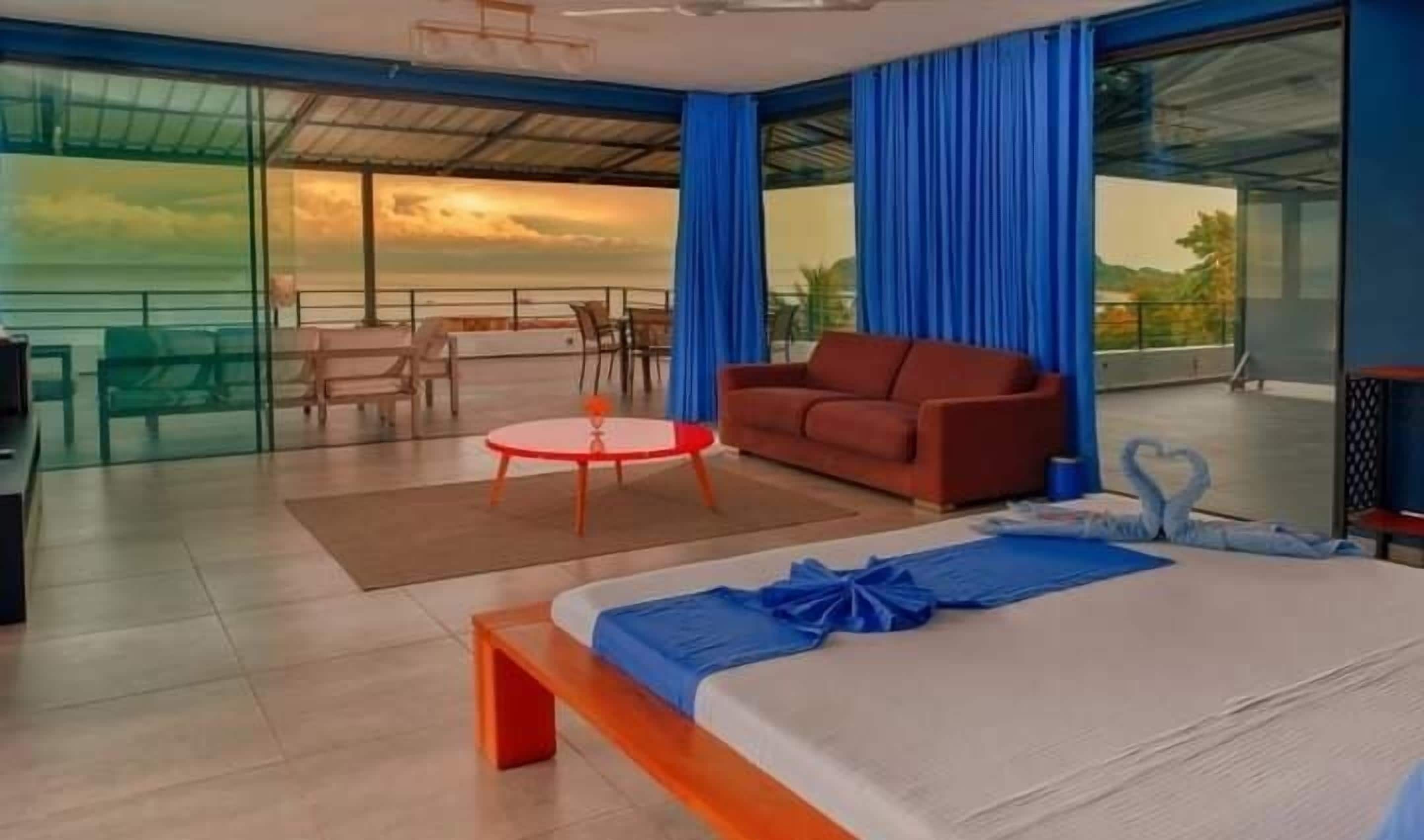 Una habitación de hotel moderna con una cama grande, un sofá rojo, una mesita redonda y un balcón con vistas.