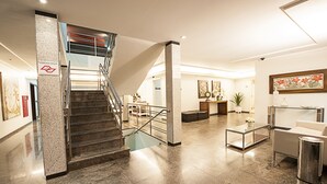 A modern lobby with a marble staircase, a reception desk, and a seating area.