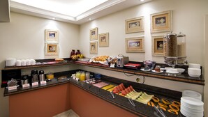 A breakfast buffet with various food items and beverages, framed pictures on the wall, and a coffee station.
