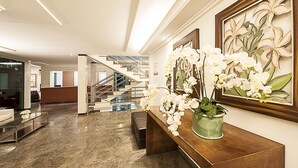 A lobby with a marble floor, a reception desk, a staircase, and a framed orchid painting.
